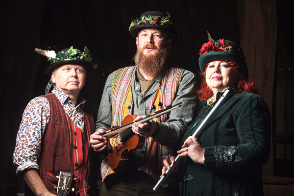 Murphy’s Lore Trio image. The trio (2 males, 1 female) are wearing hats with wild flowers / leaves / feathers on the rim. The male musicians are wearing colourful waistcoats and the female is wearing a dark green dress coat. We can see 1 musician holding a violin, another a whistle, and the third's instrument is out of shot. 
