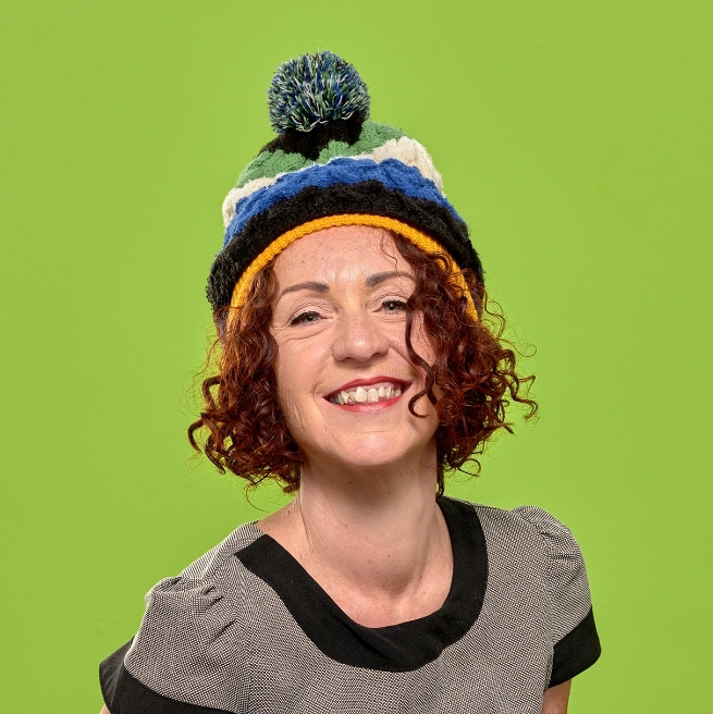 Sandi Smith image. She has short red curly hair. She is wearing a wooly hat. The image has a bright green background. 